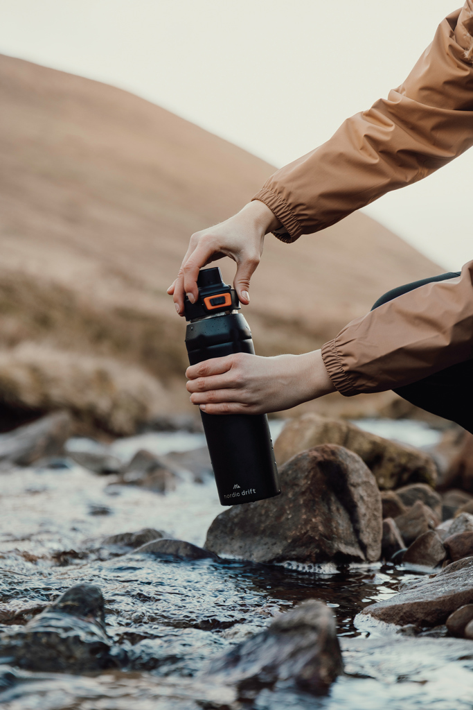 man met drinkfles met logo bij een rivier