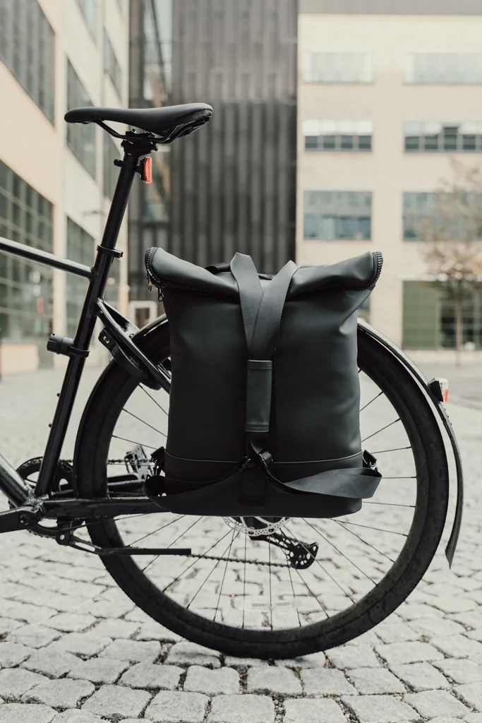 Zwarte fietstas als duurzaam en functioneel relatiegeschenk, bevestigd op een fiets in een stedelijke omgeving.